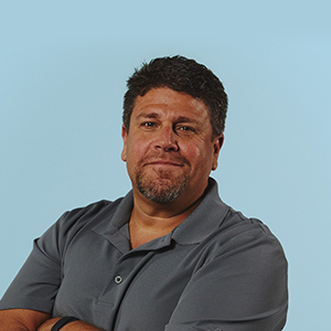 Man with big dark brown beard wearing a navy blue button shirt smiling