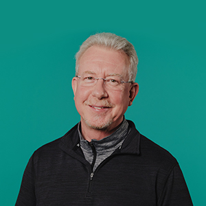 Man with white hairs wearing a blck zipper shirt smiling